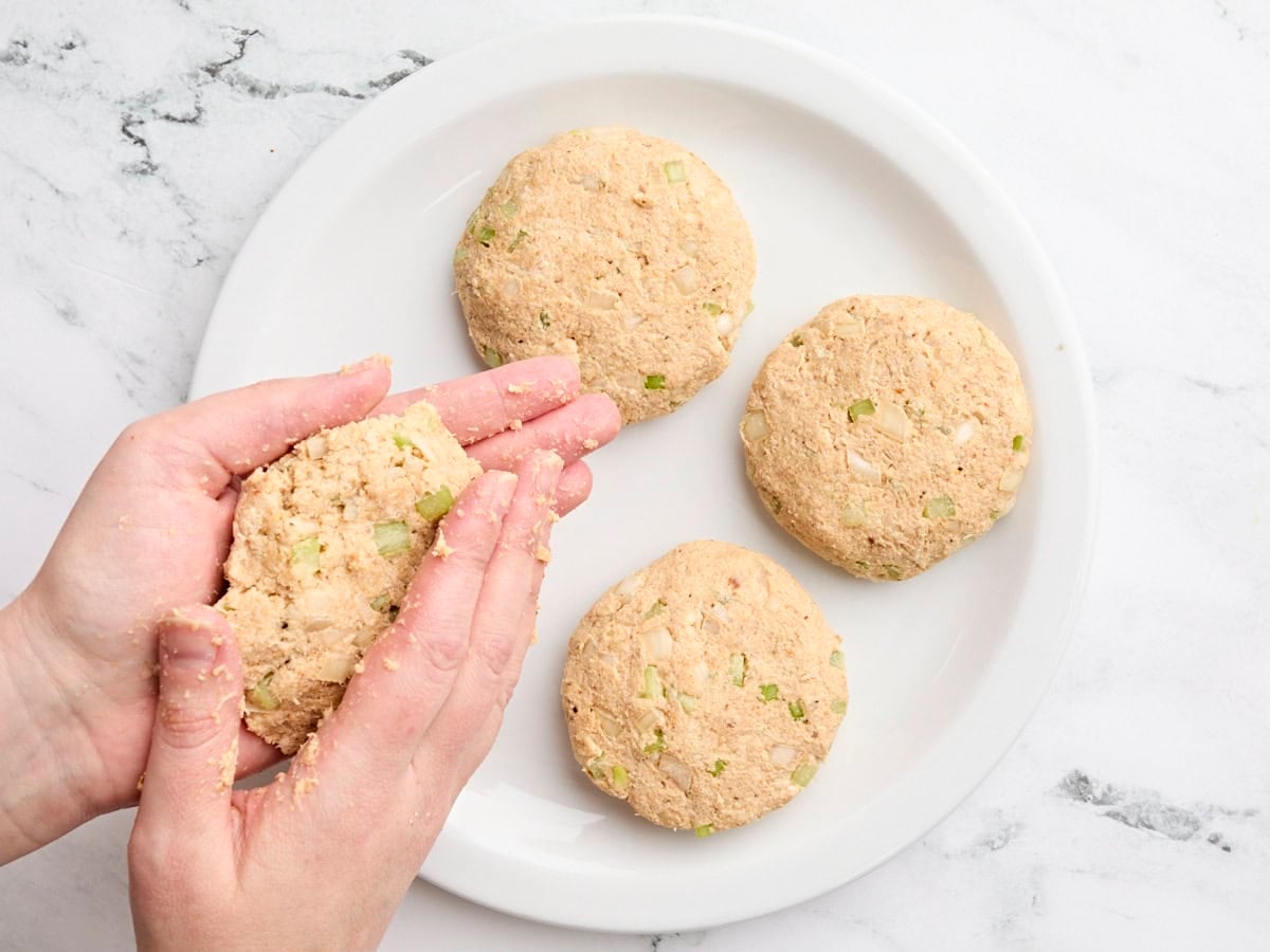 Hands forming crab cakes on a plate.