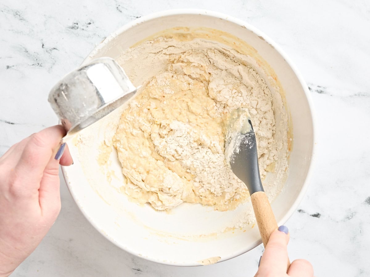 More flour being adding to a yeast and flour mixture in a bowl.