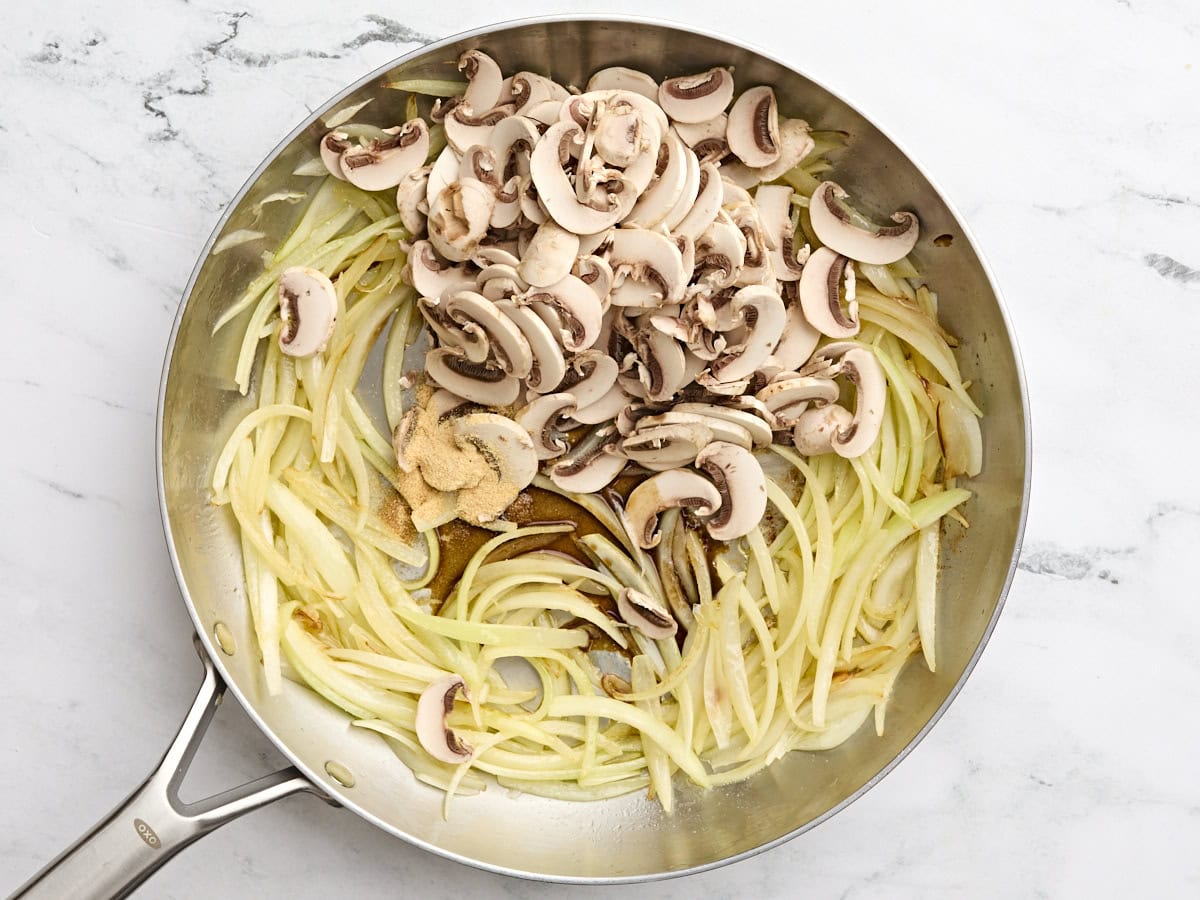 Sliced mushrooms added to sauted onions in a skillet.