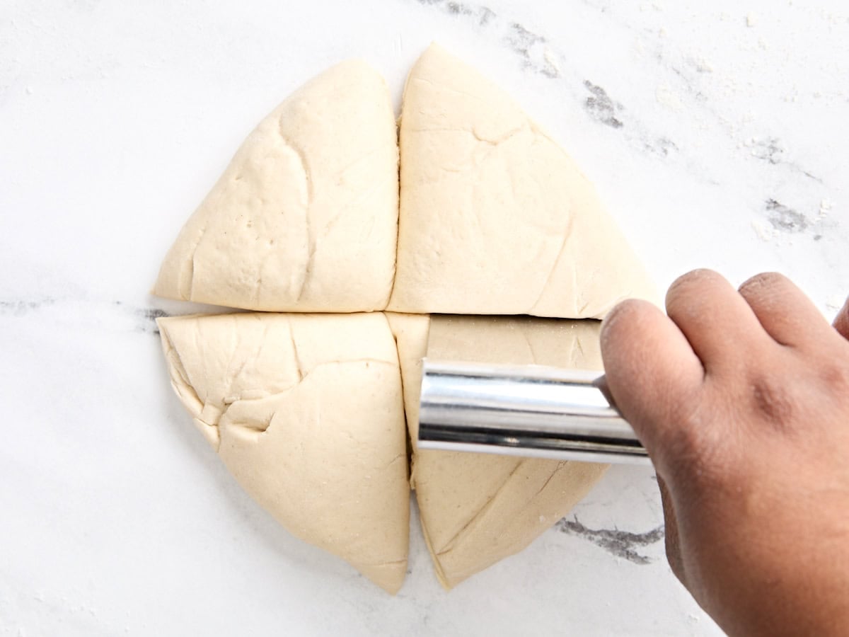A ball of pizza dough being cut into 4 portions.