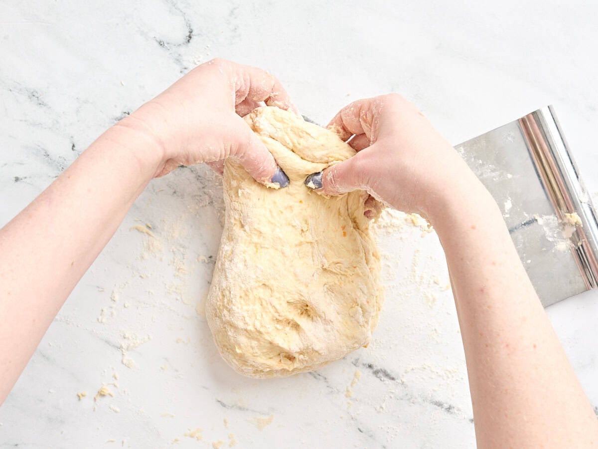 The homemade dough for orange rolls being pulled by two hands.