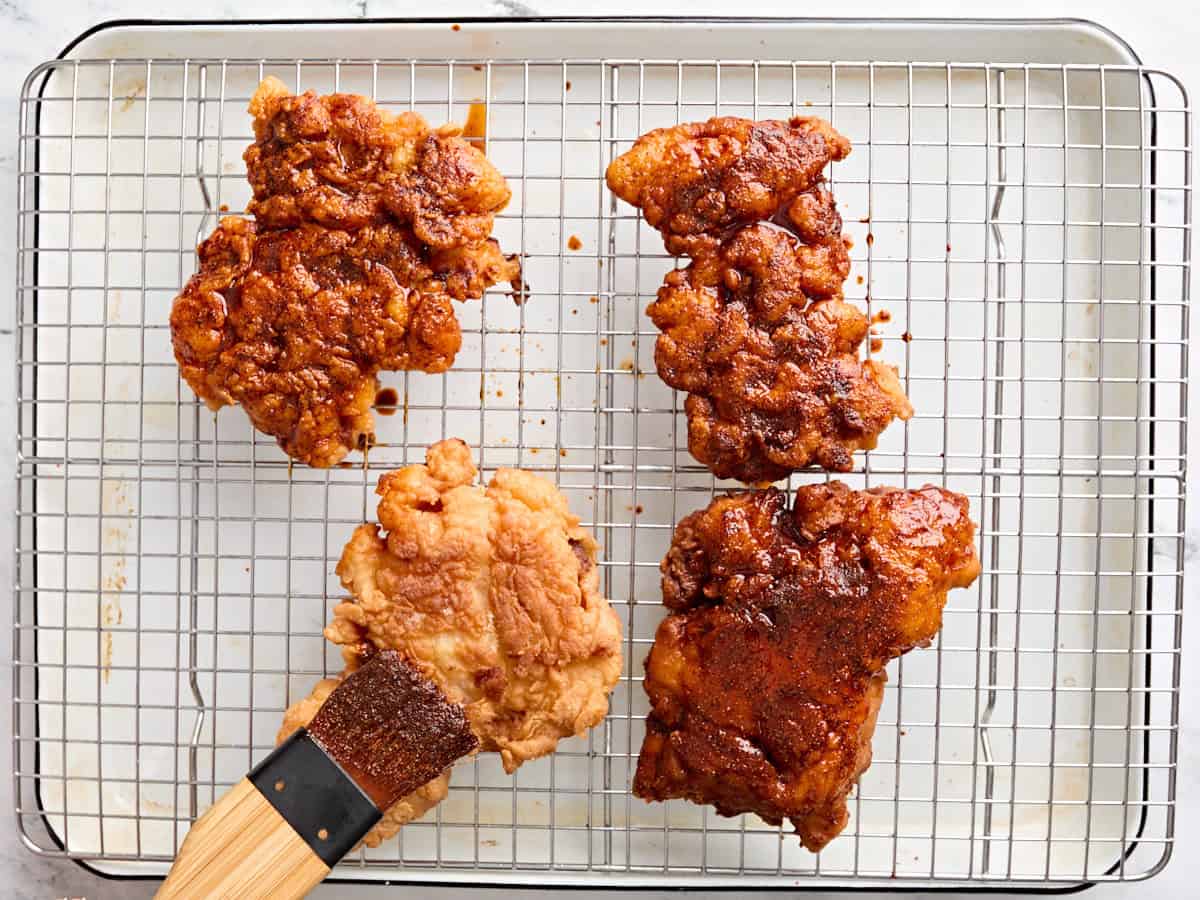 A brush covering four fried chicken thighs with a Nashville hot chicken seasoning glaze.