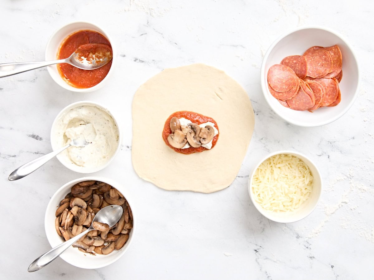 A circle of pizza dough being topping with fillings