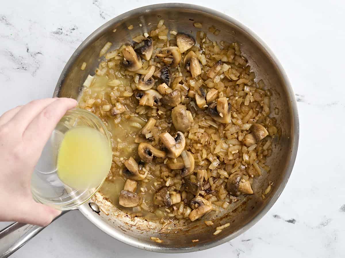 Chicken broth being added to sauteed mushrooms and onion.