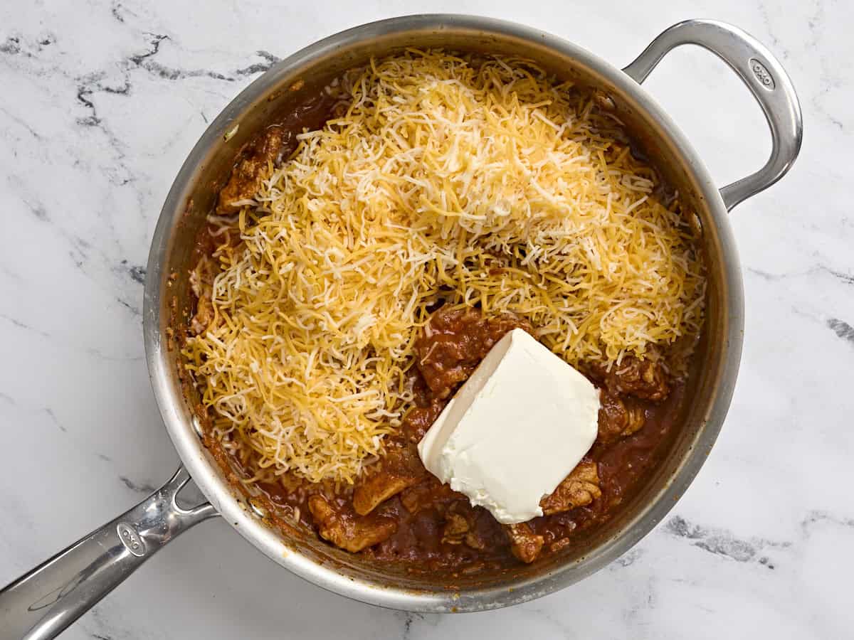 Cream cheese and shredded colby jack added to a skillet with seasoned chicken and tomato sauce.
