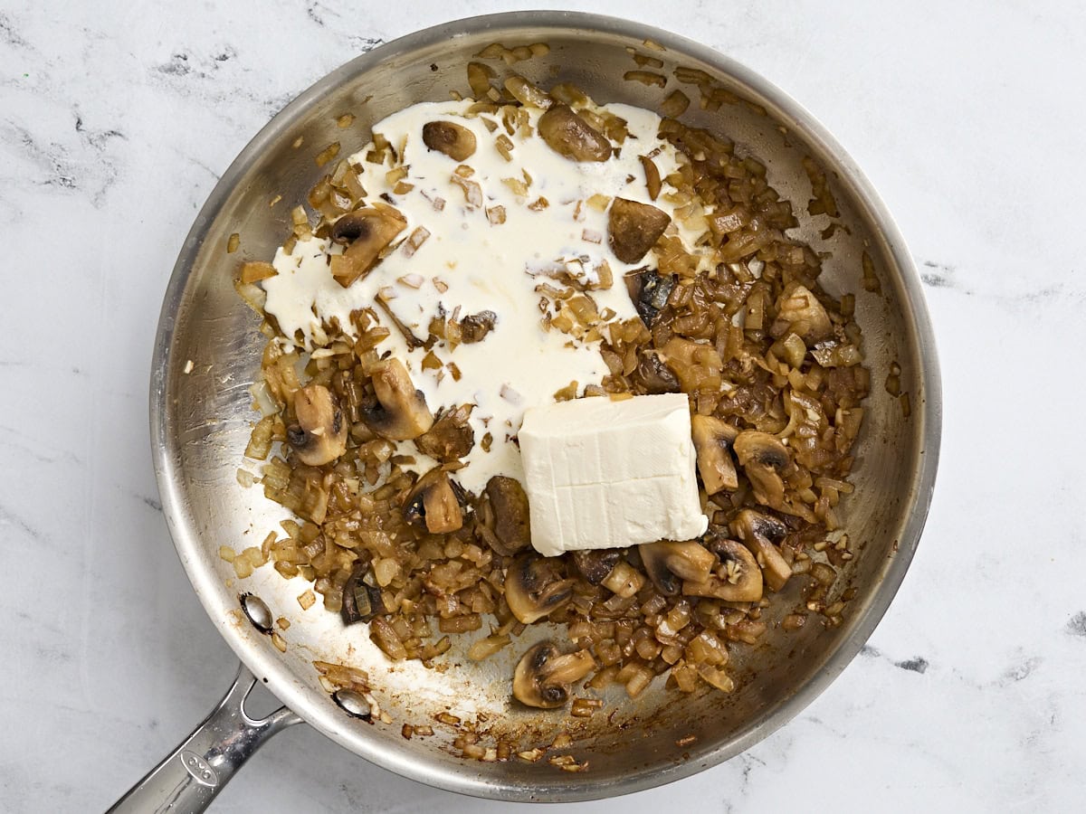 Heavy cream added to sauteed mushrooms and onions in a skillet.