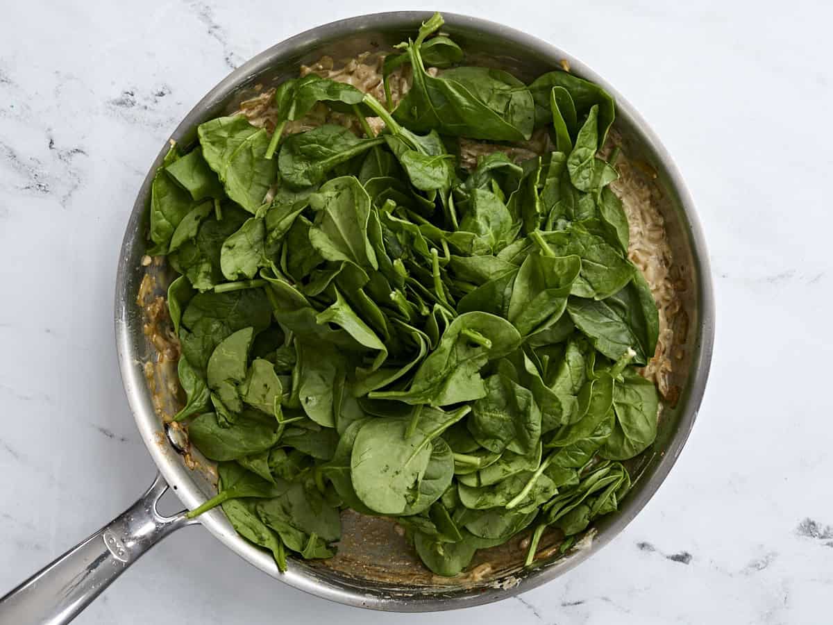 Fresh spinach added to creamy mushroom and onions in a skillet.