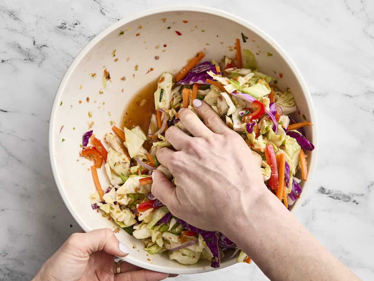 A hand massaging salt into prepped vegetables in a bowl.