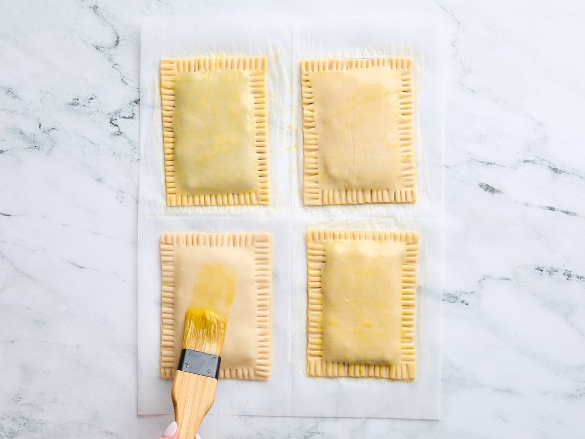 A basting brush topping four unbaked copycat pop tarts with egg wash.