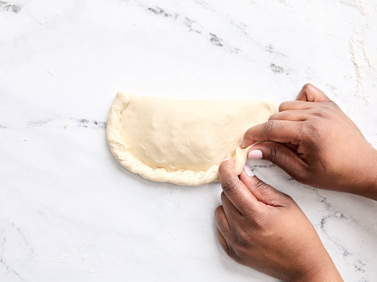 Hands crimping the edges of a calzone shut.