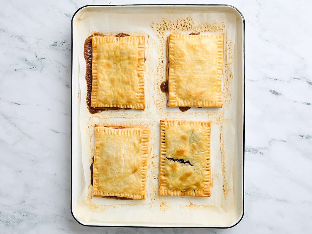 Four freshly baked pop tarts on a parchment lined baking sheet.