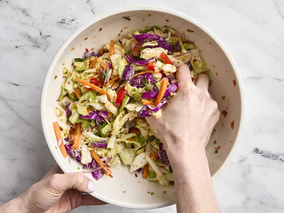 A hand massaging salt into prepped vegetables in a bowl.