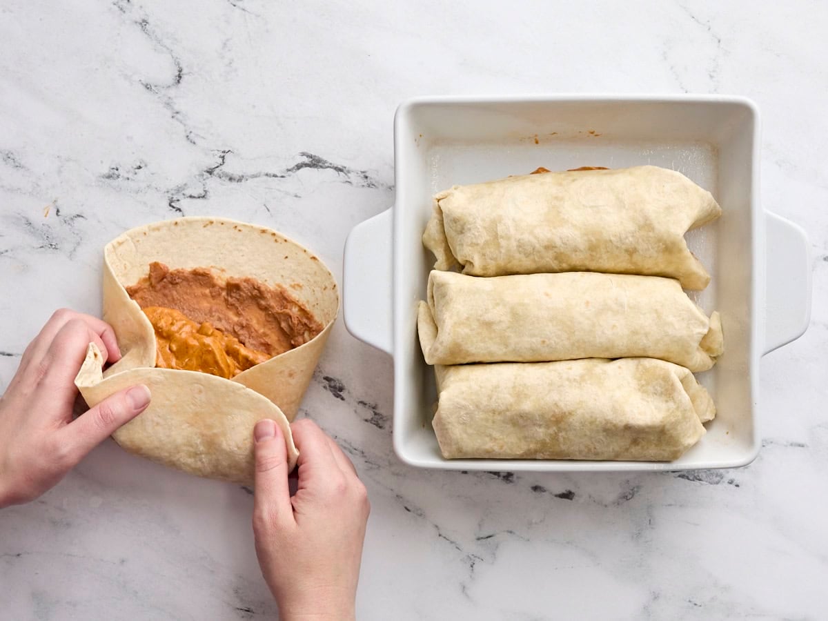 A hand folding homemade chicken chimichangas.