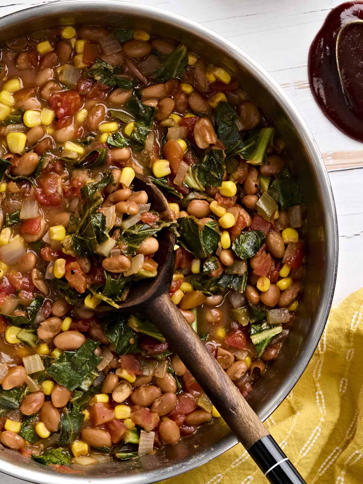 Overhead view of a skillet of bbq beans and greens with a wooden spoon.