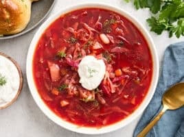 Overhead view of a bowl of borscht topped with sour cream and fresh herbs.