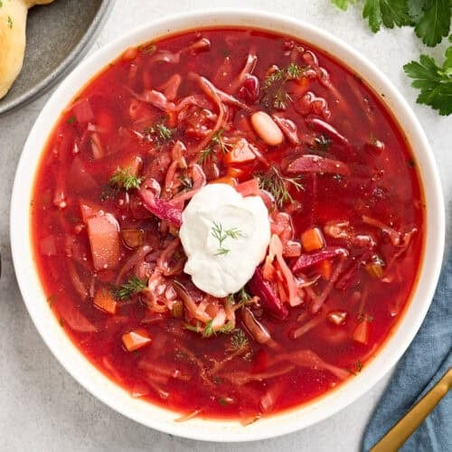 Overhead view of a bowl of borscht topped with sour cream and fresh herbs.