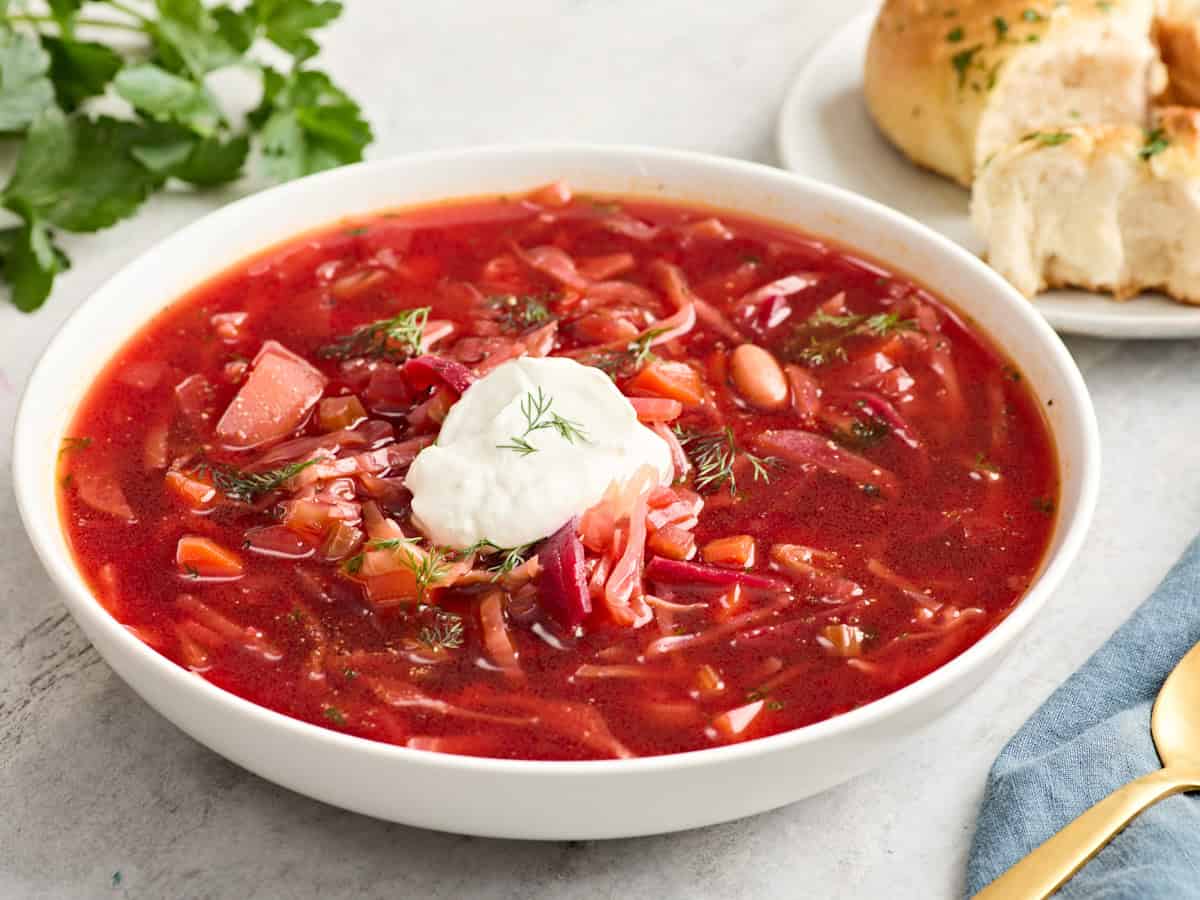 Side view of a bowl of borscht topped with sour cream.