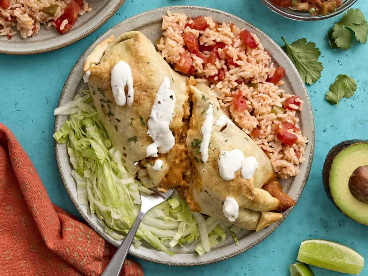 Overhead view of a baked chicken chimichanga sliced in half on a plate with Spanish rice and shredded lettuce.