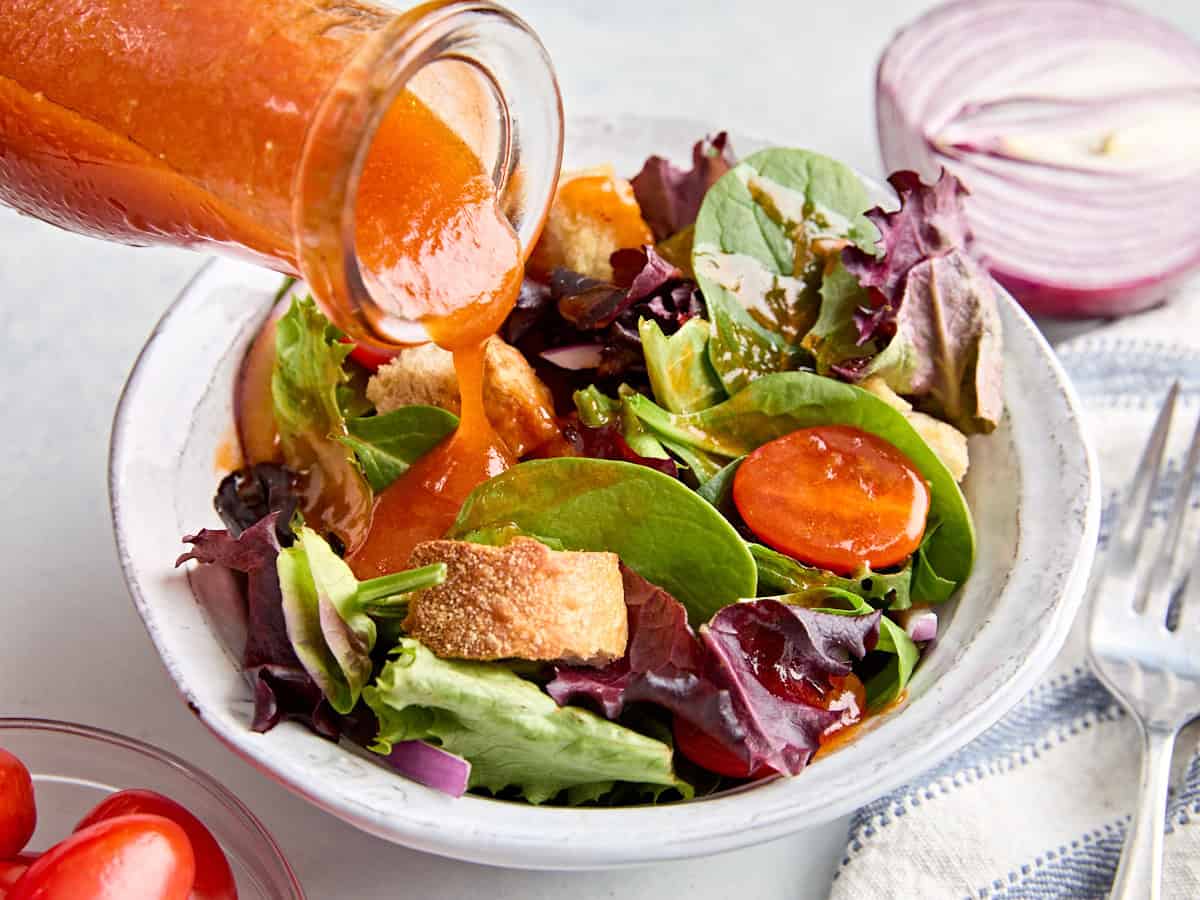 A homemade French dressing being poured over a bowl of salad.