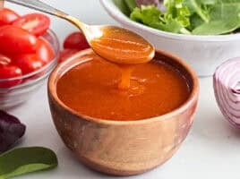 Side view of a bowl of french dressing, with a spoon taking some.
