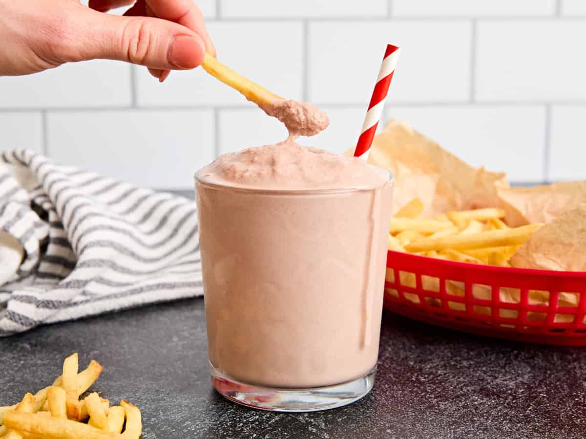A hand dipping a French fry into a glass of homemade frosty.