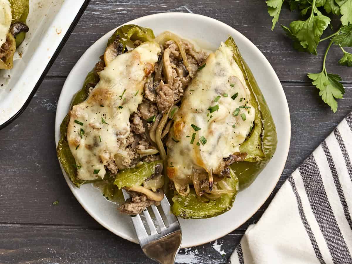 Overhead view of a philly cheesesteak stuffed pepper on a plate, cut in half, with a fork taking some of the filling.