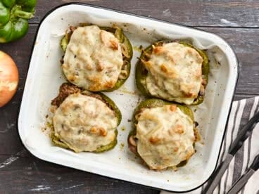 Overhead view of four philly cheesesteak stuffed peppers on a baking sheet.