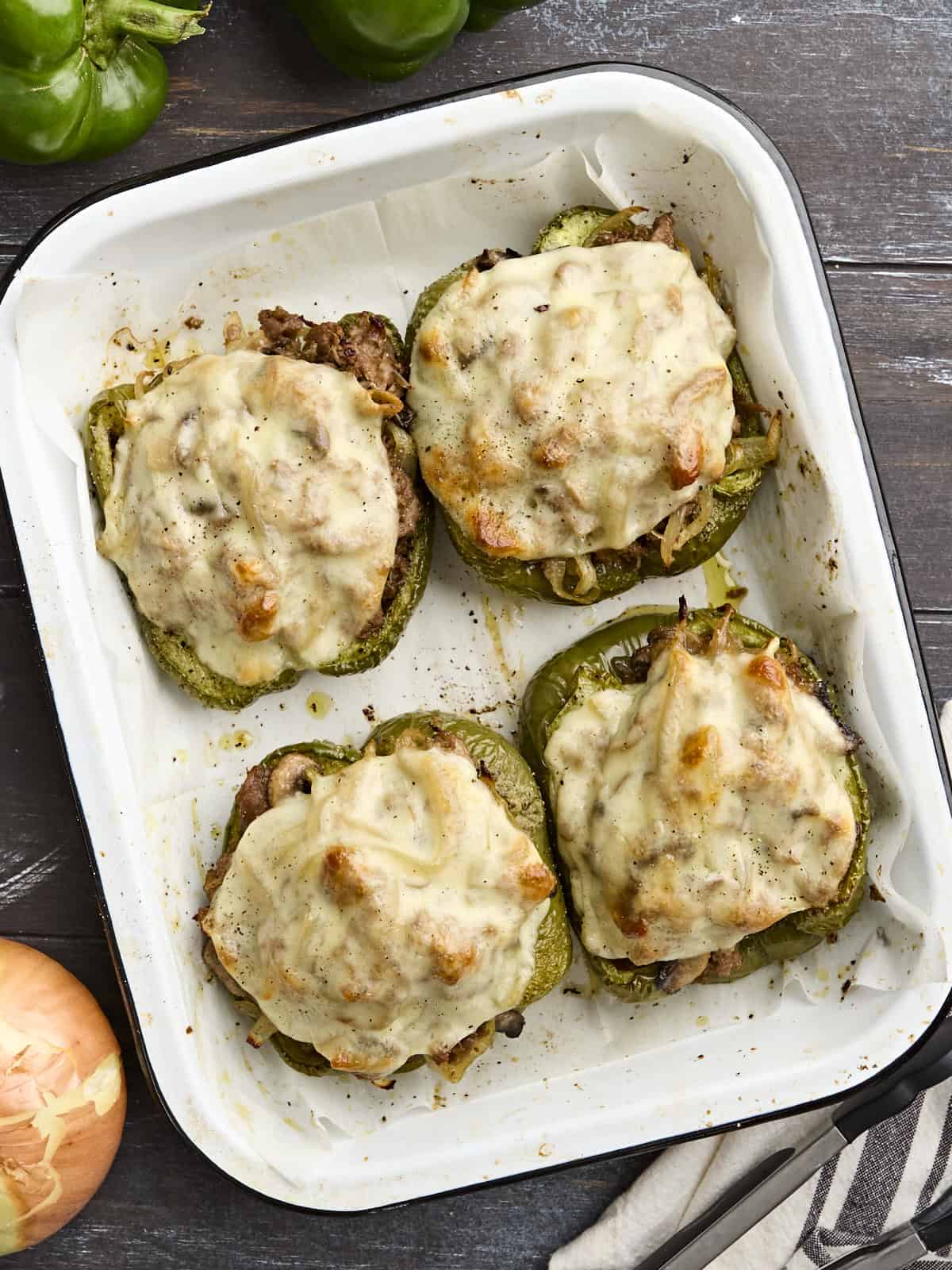 Overhead view of four philly cheesesteak stuffed peppers on a baking sheet.