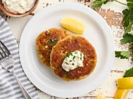 Overhead view of two homemade crab cakes on a plate with a lemon wedge and tartar sauce.
