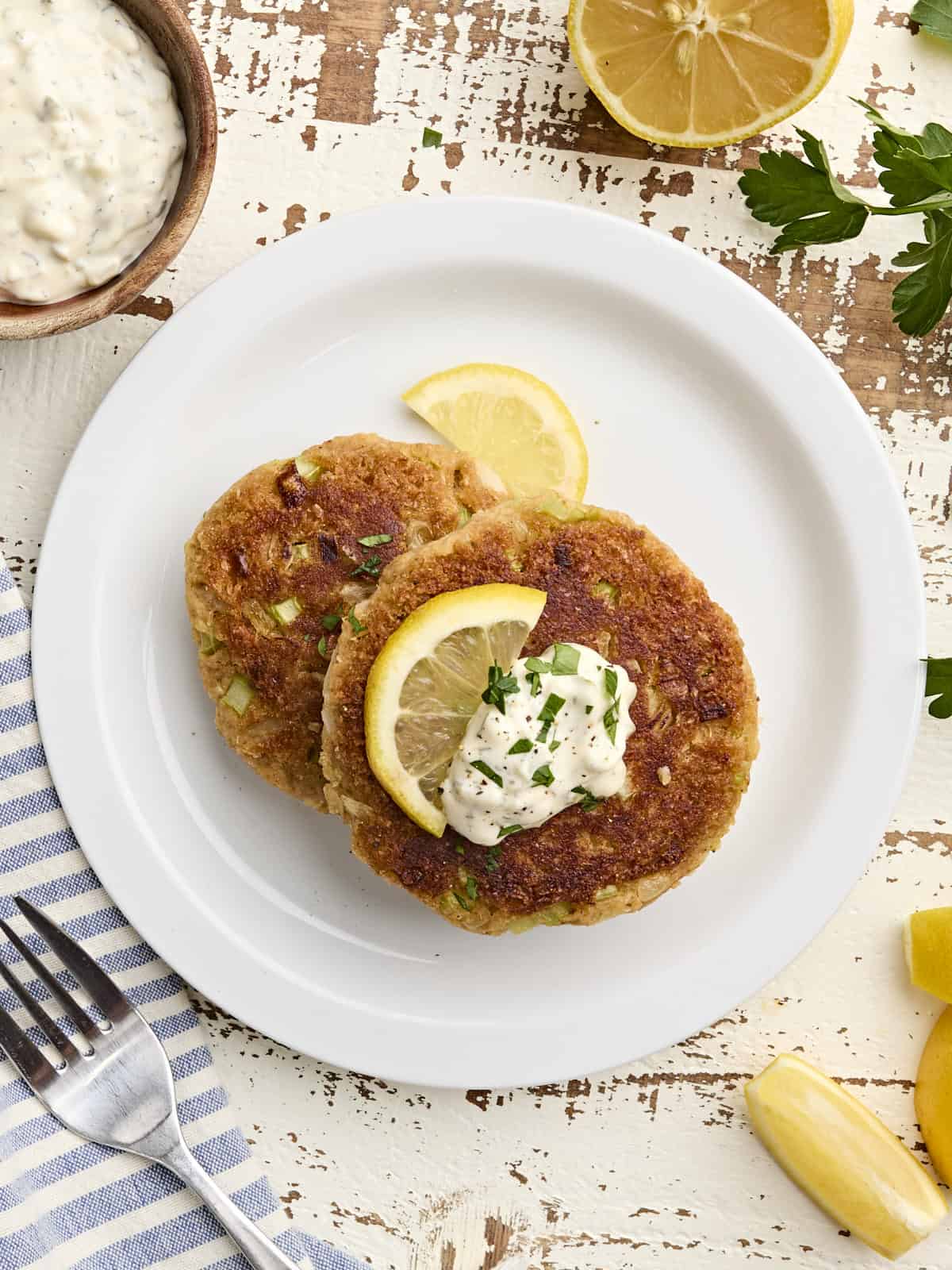 Overhead view of two homemade crab cakes on a plate with a lemon wedge and tartar sauce.