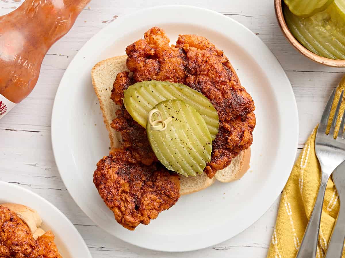 Overhead view of plated homemade Nashville hot chicken on Texas bread with sliced pickles.