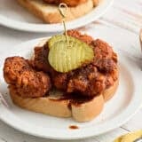 Side view of homemade Nashville hot chicken on a slice of Texas bread on a plate and topped with pickle slices.