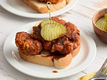 Side view of homemade Nashville hot chicken on a slice of Texas bread on a plate and topped with pickle slices.