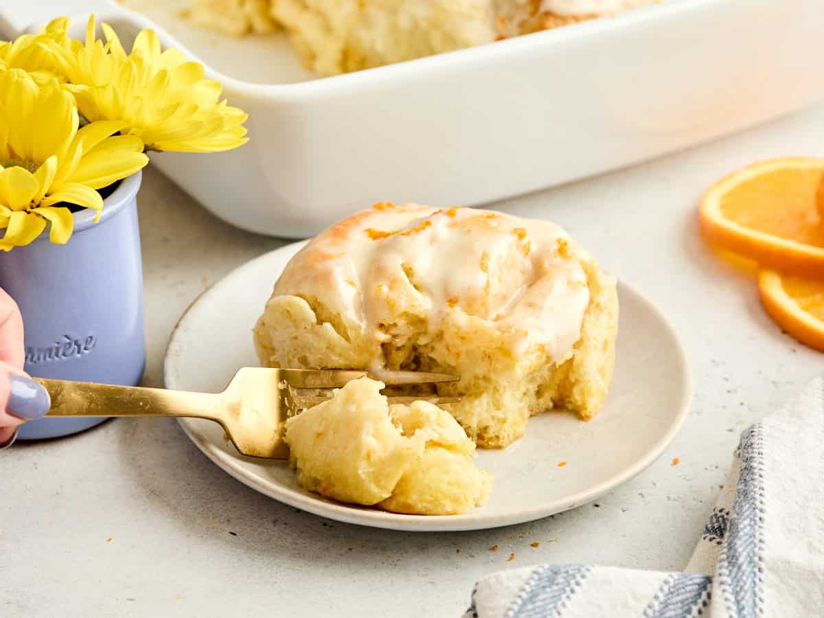 An orange roll on a plate, being cut into by a fork.