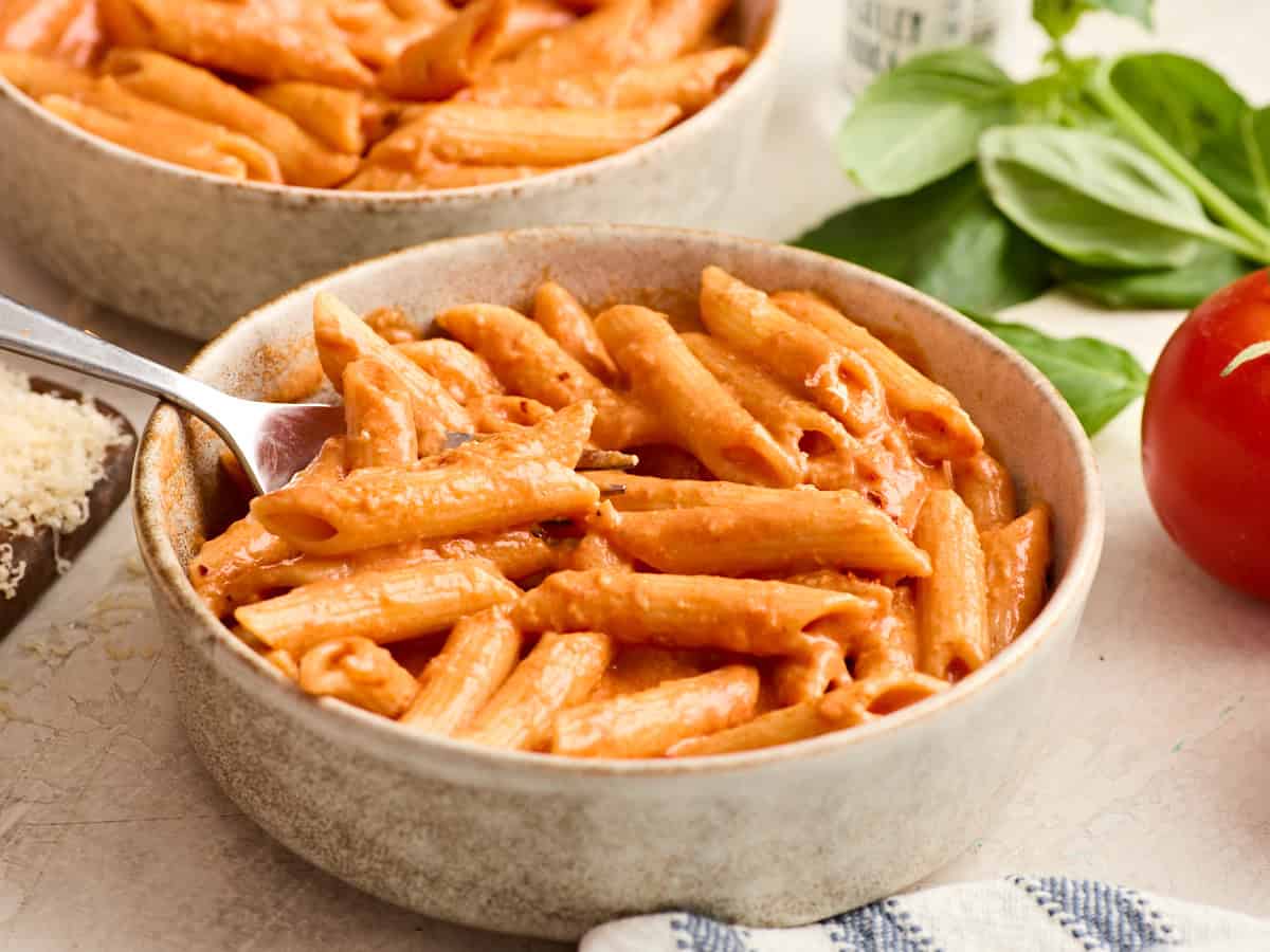 Side view of a bowl of pasta and vodka sauce with a fork taking some.