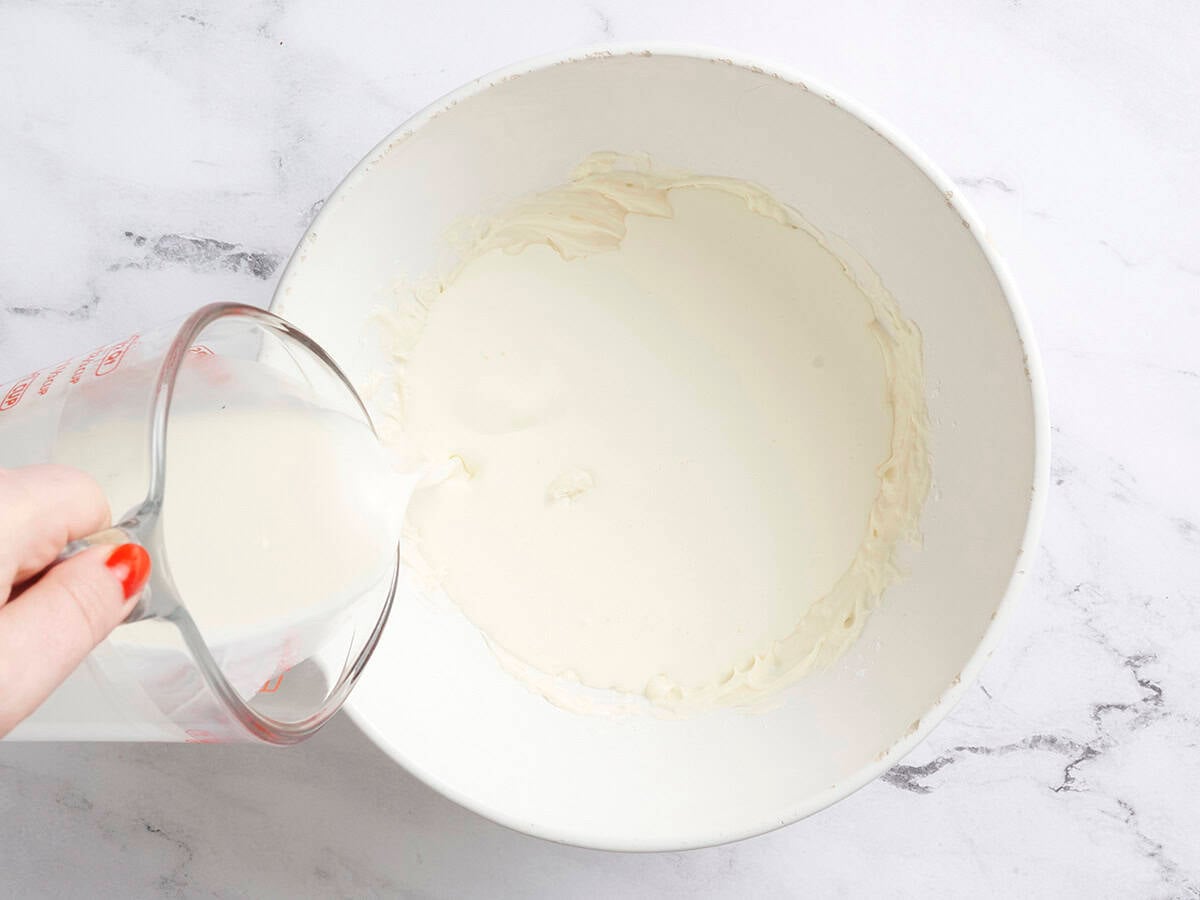 Heavy cream being poured into a bowl with whipped cream cheese.