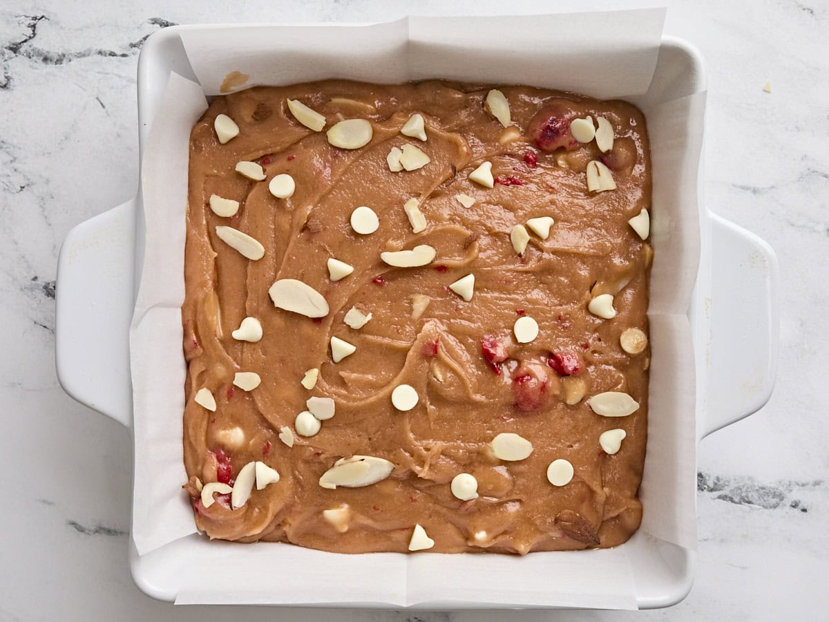 The batter for cherry blondies in a lined baking dish.