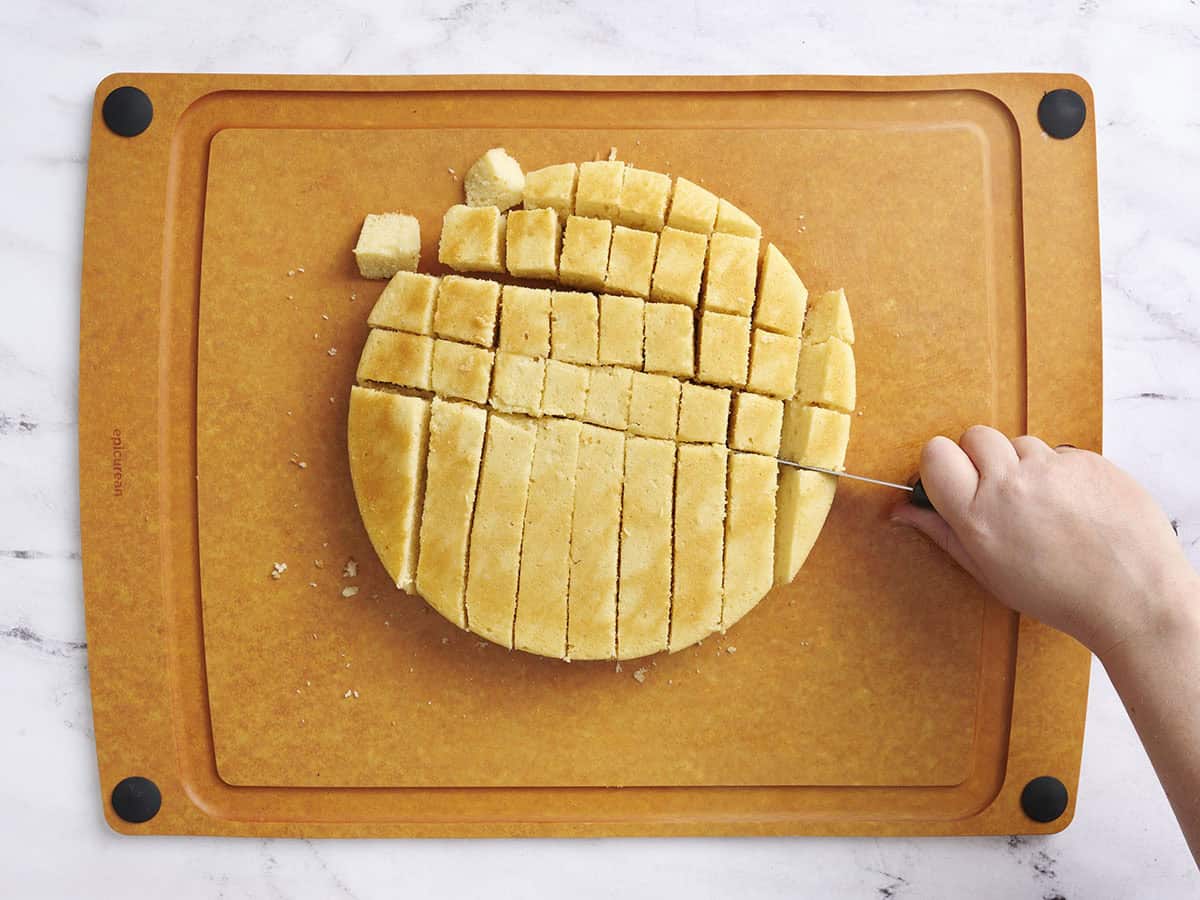A vanilla cake being sliced into cubes.