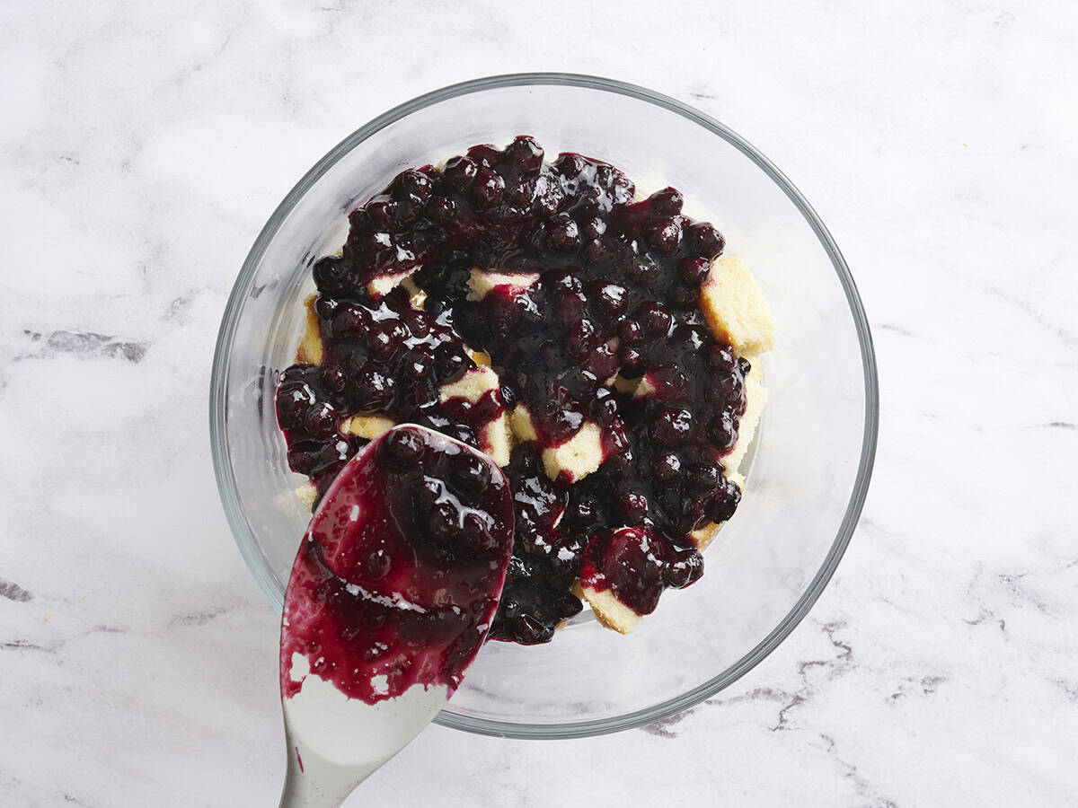 Blueberry sauce layer added to vanilla cake cubes in a trifle dish.