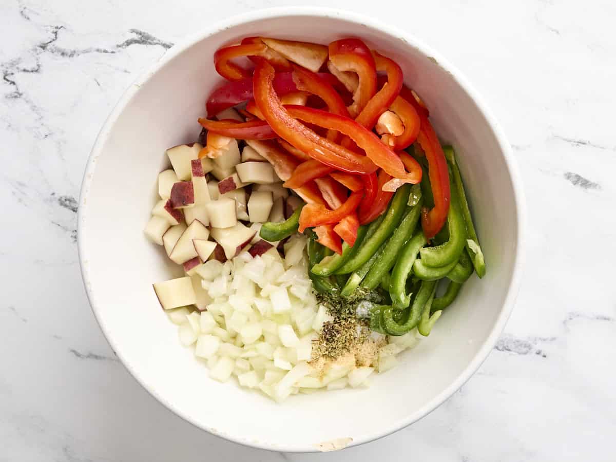 Sliced peppers potatoes and onion in a mixing bowl.