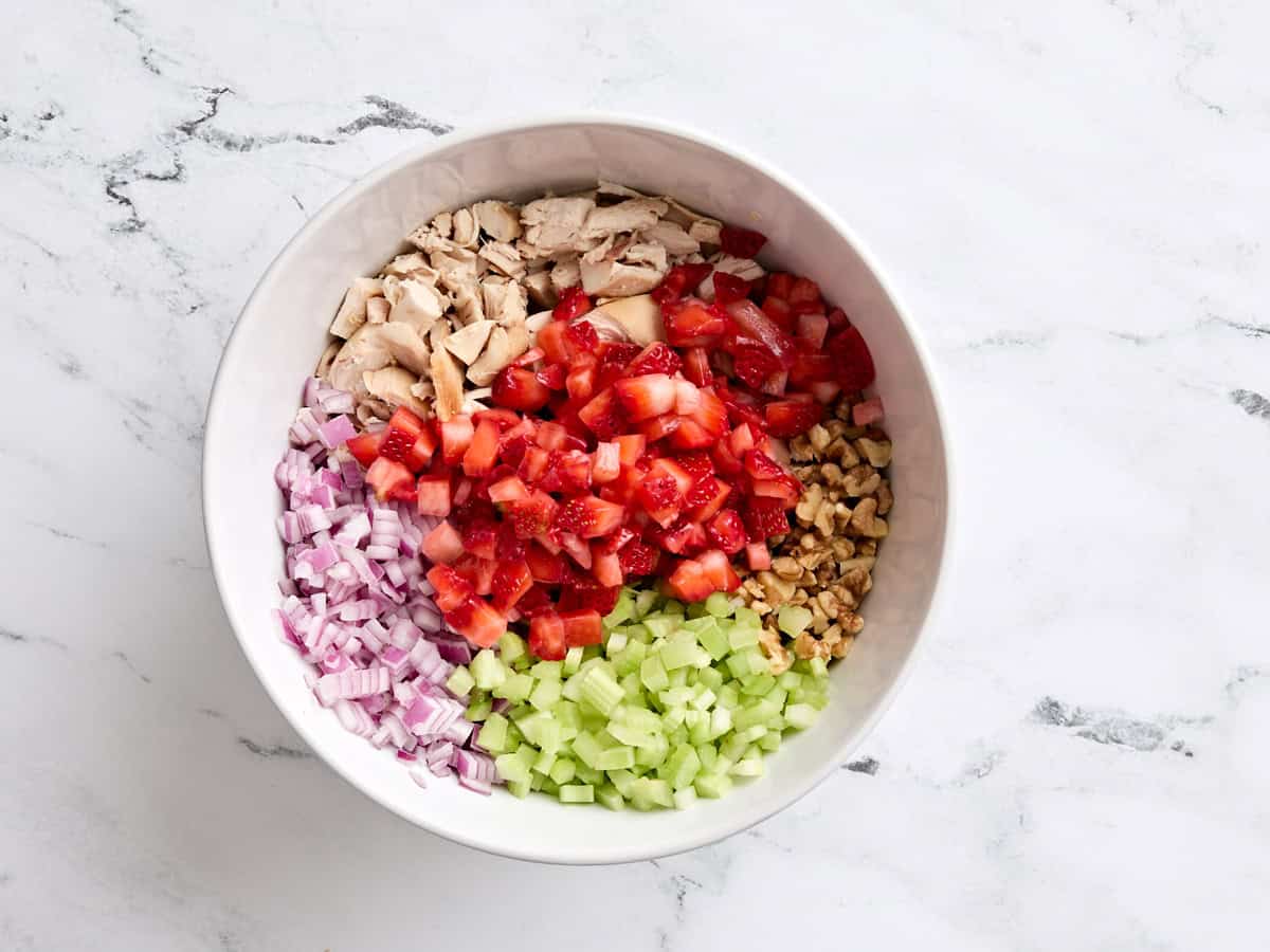 Shredded chicken, diced strawberries, diced onion, diced walnuts, and diced celery in a mixing bowl.