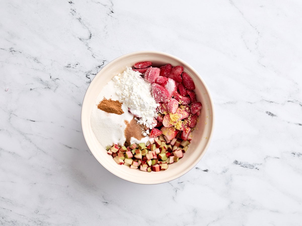 Frozen strawberries, chopped rhubarb, lemon zest, cornstarch, sugar, and seasonings in a mixing bowl.
