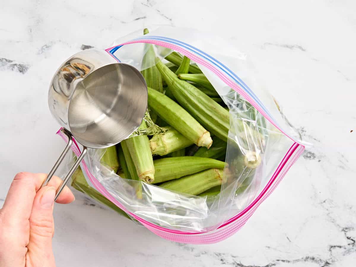 Fresh okra in a ziplock bag with vinegar being poured in.