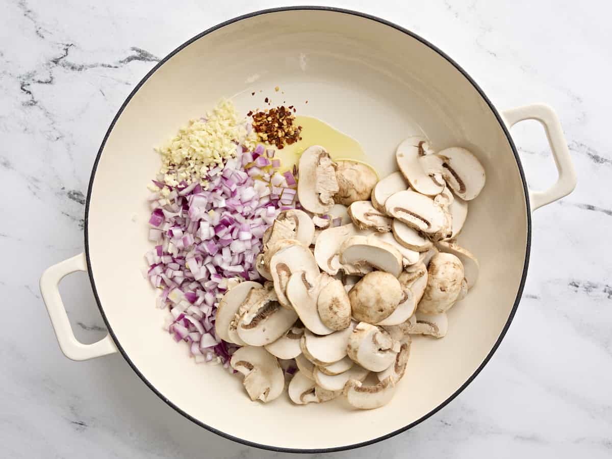 Diced red onion, sliced mushrooms, garlic, and crushed red pepper in a skillet.