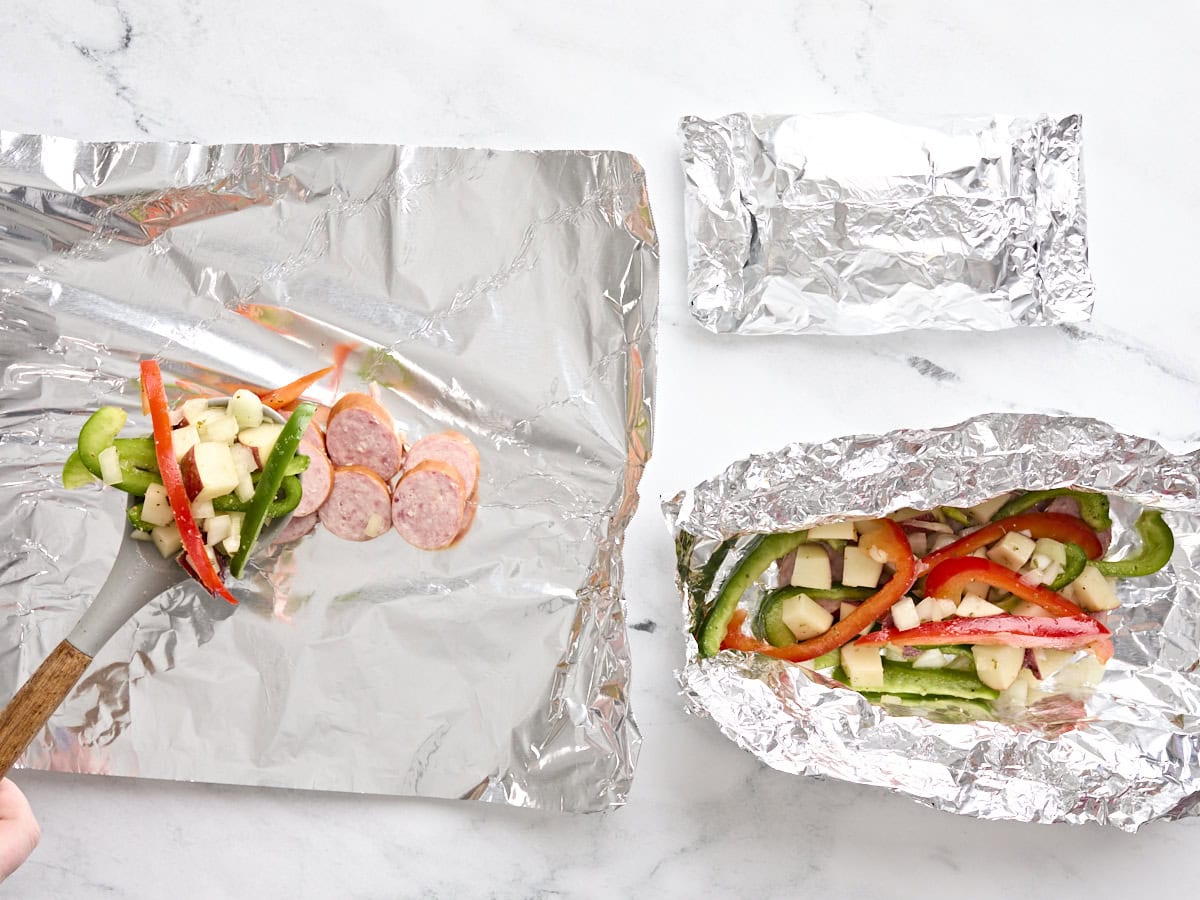 A sausage and vegetable mix being divided between three foil packets.