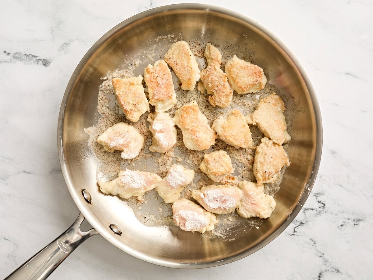 Diced chicken breast cooking in a skillet.