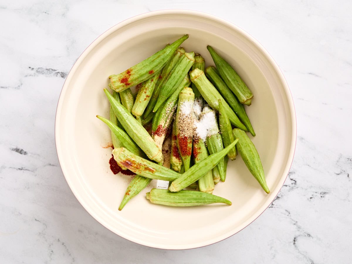 Fresh okra in a mixing bowl with seasonings.