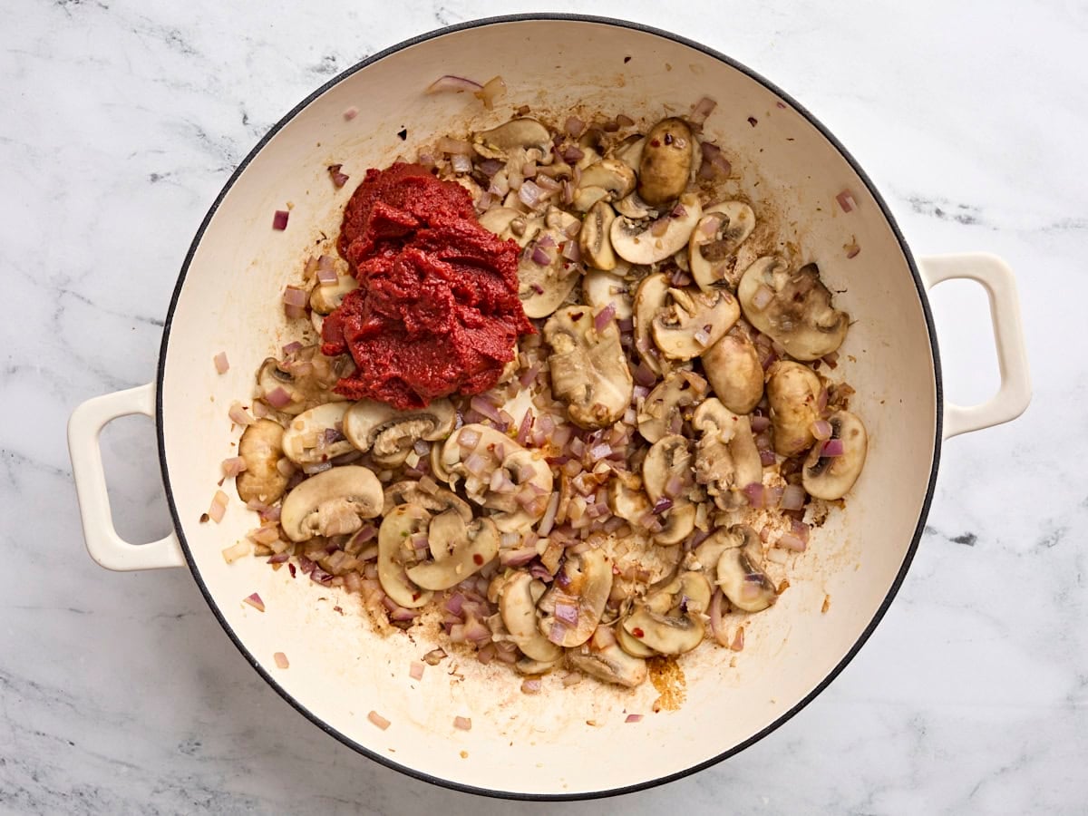 Sauteed mushrooms in a skillet with tomato paste.
