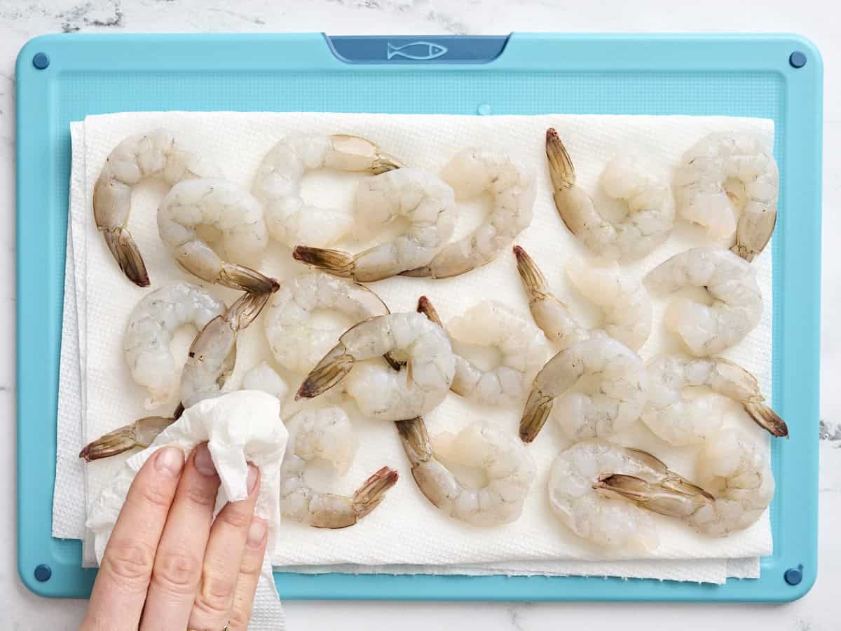 A hand patting dry raw shrimp.