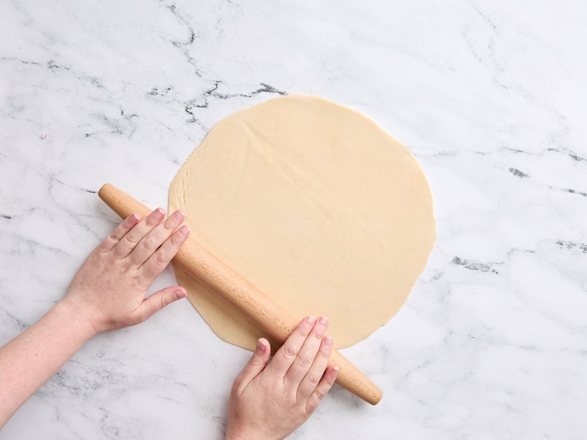 Hands using a rolling pin to roll out a pie crust.